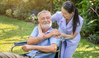 Happy nurse holding elderly man hand on wheelchair in garden at