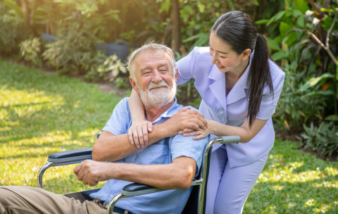Happy nurse holding elderly man hand on wheelchair in garden at