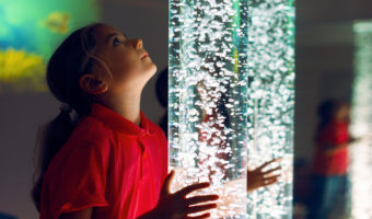 Child in therapy sensory stimulating room, snoezelen. Child interacting with colored lights bubble tube lamp during therapy session.