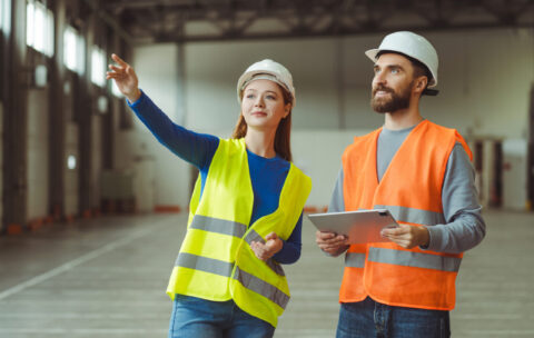 Successful workers, engineers, wearing protective workwear and safety helmets, using digital tablet