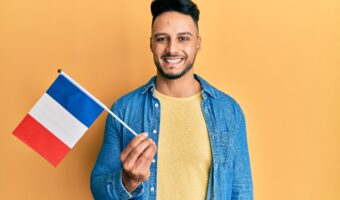 Young arab man holding france flag looking positive and happy standing and smiling with a confident smile showing teeth