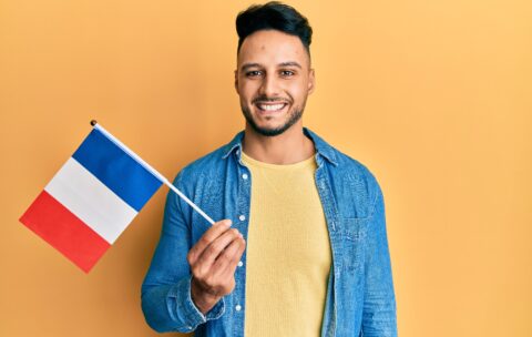 Young arab man holding france flag looking positive and happy standing and smiling with a confident smile showing teeth