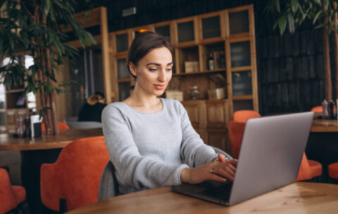 Woman sitting in a cafe drinking coffee and working on a computer