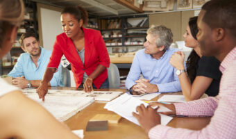 Female Boss Leading Meeting Of Architects Sitting At Table
