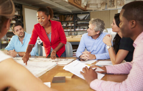 Female Boss Leading Meeting Of Architects Sitting At Table