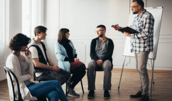 Handsome senior professional therapist stands in front of a group of people of different ages during meeting for people with social problems