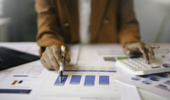Businesswoman analyzing financial charts and using calculator in office