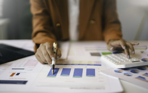 Businesswoman analyzing financial charts and using calculator in office