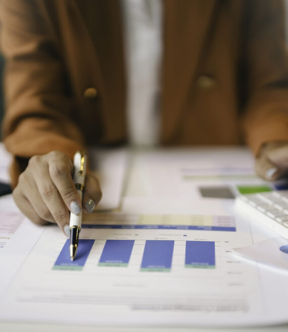 Businesswoman analyzing financial charts and using calculator in office