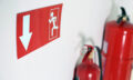 Emergency exit sign and fire extinguishers on white wall, closeup