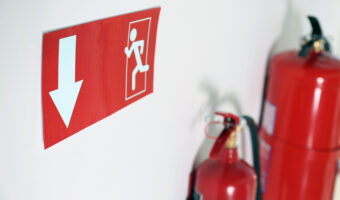 Emergency exit sign and fire extinguishers on white wall, closeup