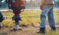 technician installing ground screw for mounting structure of solar panel at solar farm