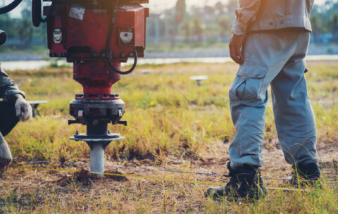 technician installing ground screw for mounting structure of solar panel at solar farm