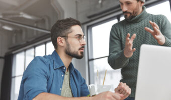 Professional satisfied finance workers collaborate in friendly atmosphere, discuss something actively, develop new startup, sit in front of laptop computer at spacious cabinet, check online project