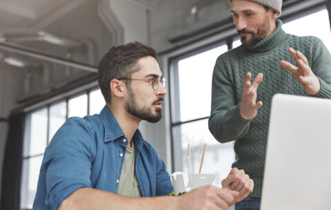 Professional satisfied finance workers collaborate in friendly atmosphere, discuss something actively, develop new startup, sit in front of laptop computer at spacious cabinet, check online project