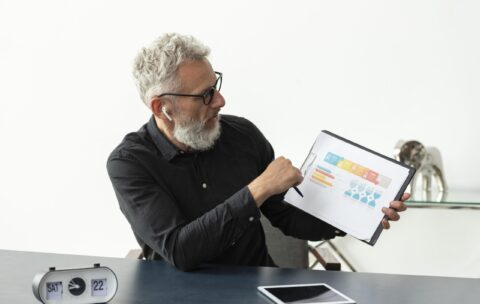 older-man-home-showing-graph-notepad-with-tablet-desk (1)